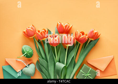 Easter flat lay on orange paper. Painted  eggs, gift cards, envelopes and gift boxes. Stock Photo