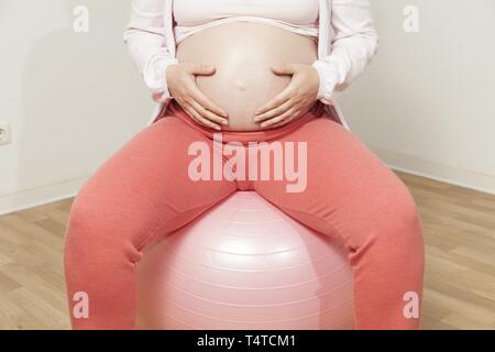 Pregnant woman sitting on exercise ball and has hands on baby belly Stock Photo