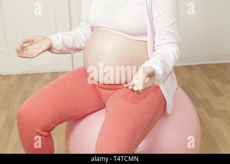 Pregnant woman sitting on an exercise ball and meditating Stock Photo