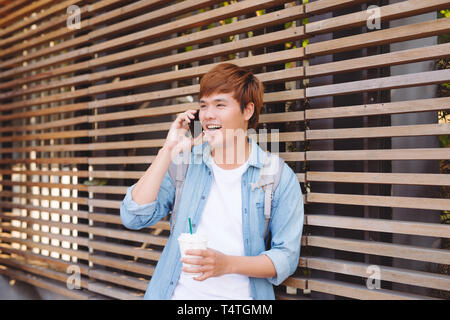 Young asian man smiling and talking on mobile phone outside with copy space on the left Stock Photo
