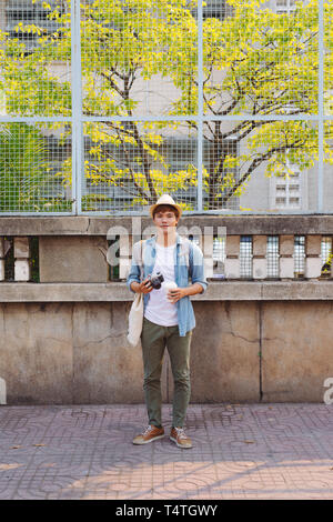 Young Asian man traveler and photographer with jean shirt and hat taking photos Stock Photo
