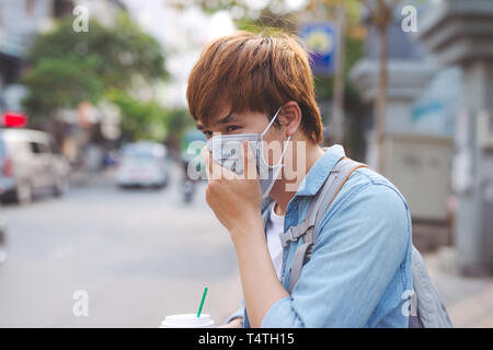 Asian man in the street wearing protective masks., Sick man with flu wearing mask and blowing nose into napkin as epidemic flu concept on the street. Stock Photo