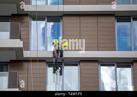 Mountain climber washes windows. Worker using rope to clean a high apartment building, steeplejack works. Stock Photo