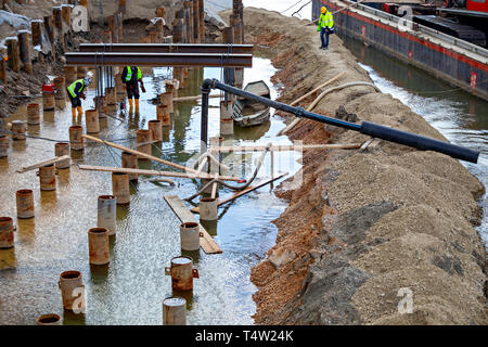 Workers welding and grinding in wet conditions. Abstract: Dangers of welding around water, not following standard safety procedure. Stock Photo