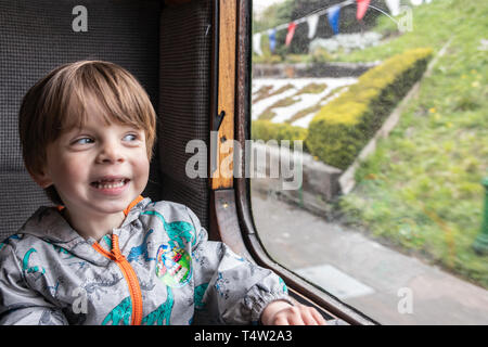 Smiling two year old boy looking out of an old train carriage window Stock Photo