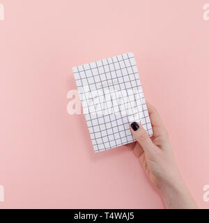 Top view of woman hand with stylish black manicure holding notepad with copy space on pink color paper background in minimal style. Template for femin Stock Photo