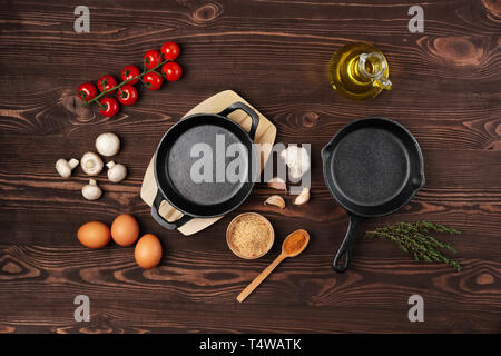 Cast iron skillets and spices on dark wooden culinary background, view from above Stock Photo