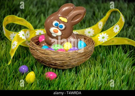 chocolate Easter rabbit in bird nest with colorful eggs on green grass and yellow ribbon Stock Photo