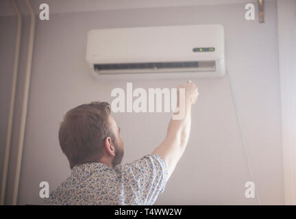 one young man, 20-29 years old, turning on his air conditioner. rear view. Stock Photo