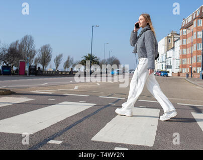 Teenage girl walking across a zebra crossing on her mobile phone Stock Photo