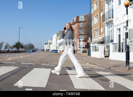 Teenage girl walking across a zebra crossing on her mobile phone Stock Photo