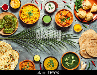 Indian cuisine dishes: tikka masala, dal, paneer, samosa, chapati, chutney, spices. Indian food on gray background. Assortment indian meal with copy space for text in center. Top view or flat lay. Stock Photo