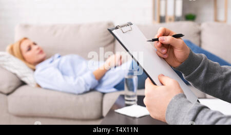Psychologist listening to depressed patient and writing down notes Stock Photo