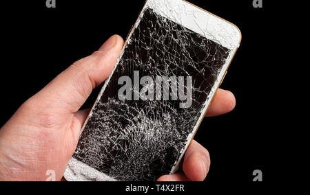 Modern smartphone with highly broken screen in men hand on black background. Stock Photo