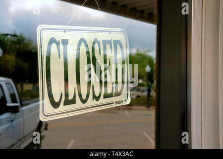 Plastic closed sign on the inside of a glass window in a storefront in Bryan, Texas, USA; reflection of parked truck on window. Stock Photo