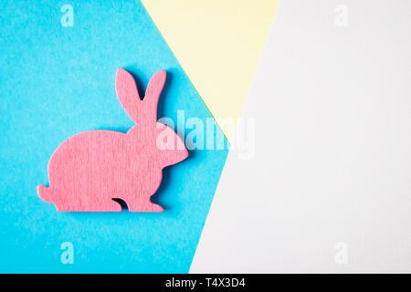 Happy Easter. Pink wooden Easter bunny on a blue and white and yellow background. Trendy creative photo Stock Photo