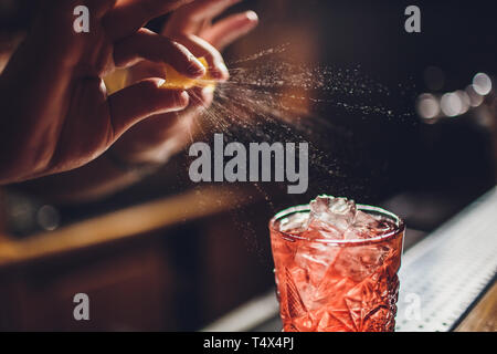 Barman s hands sprinkling the juice into the cocktail glass filled with alcoholic drink on the dark background. Stock Photo