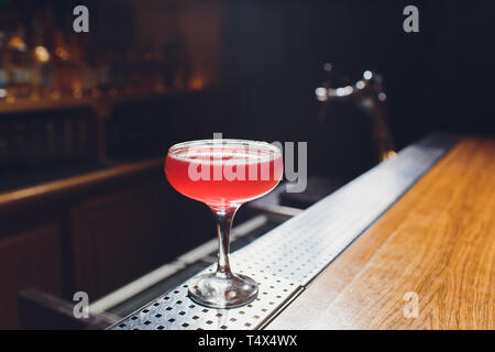 Cocktail glass with drink in the bar with bottles in the dark background. Stock Photo