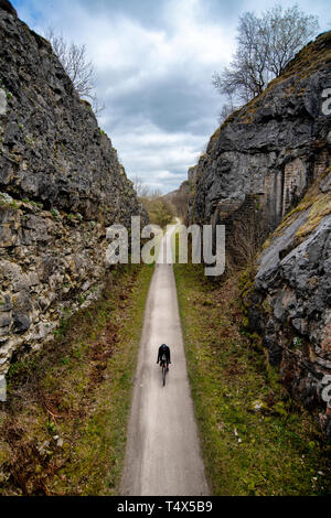 A man rides a bicycle through a cutting along the Monsal Trail in the Derbyshire Peak District. Stock Photo