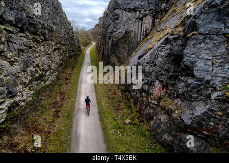 A man rides a bicycle through a cutting along the Monsal Trail in the Derbyshire Peak District. Stock Photo