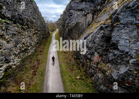 A man rides a bicycle through a cutting along the Monsal Trail in the Derbyshire Peak District. Stock Photo