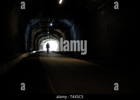 A man rides a bicycle through a tunnel along the Monsal Trail in the Derbyshire Peak District. Stock Photo