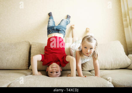 Brother and sister playing on the couch: the boy stands upside down.