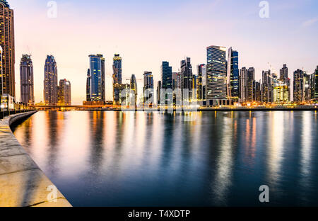 Stunning view of the illuminated Dubai skyline during sunset buildings and skyscrapers reflected on a silky smooth water flowing in the foreground. Stock Photo