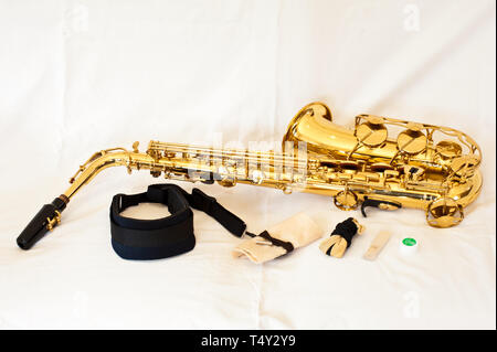 A gold / brass alto saxophone on white background with pearl keys - laid out with accessories including strap, cleaner, reed and cork grease Stock Photo