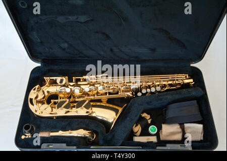 A gold / brass alto saxophone on white background with pearl keys - laid out in case with accessories including strap, cleaner, reed and cork grease Stock Photo