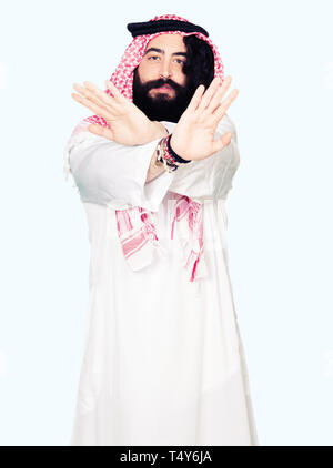 Arabian business man with long hair wearing traditional keffiyeh scarf Rejection expression crossing arms and palms doing negative sign, angry face Stock Photo