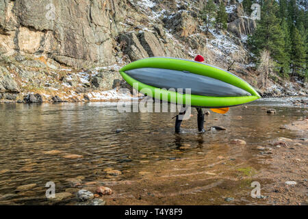 paddler carrying inflatable whitewater kayak on a shore of mountain river in early spring - Poudre River above Fort Collns, Colorado Stock Photo