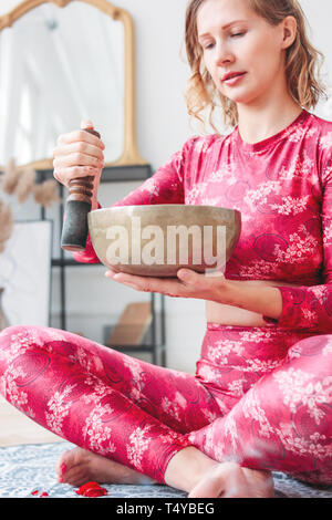 Young woman playing on brass Tibetan singing bowl. Sound therapy and meditation Stock Photo