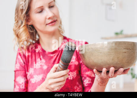 Young woman playing on brass Tibetan singing bowl. Sound therapy and meditation Stock Photo