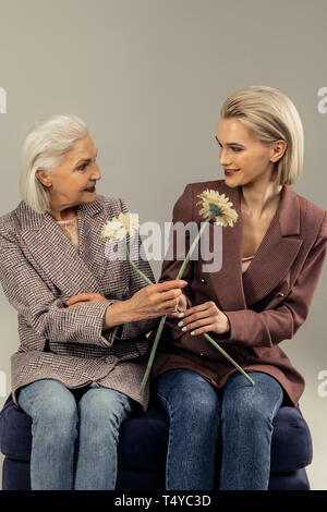 Positive delighted women giving each other flowers Stock Photo
