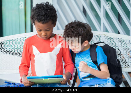 Two boy kid sitting on bench and playing game on tablet at preschoo,Kindergarten school education concept.diversity children. Stock Photo