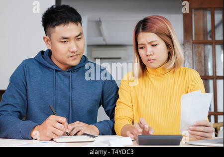Stressed Asian couple serious calculate home financial bill budget on table in kitchen at new house Stock Photo