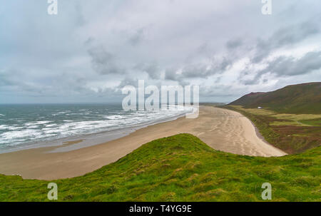 Waves pounding the beach at Rhossili Bay on the Gower Peninsula of Wales, on a windy grey Summers day in August. South Wales. Stock Photo