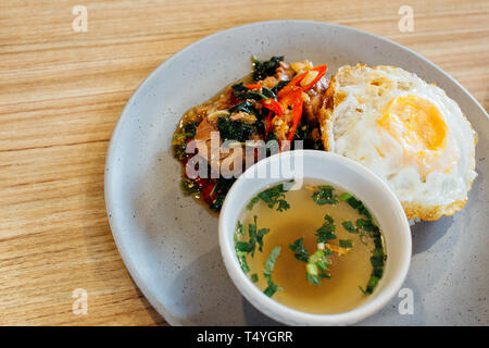 Thai basil braised pork topped with fried egg and rice along with soup on table Stock Photo