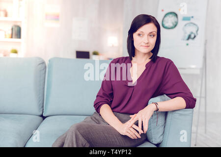 Beautiful dark-haired elegant woman sitting on a living room couch. Stock Photo