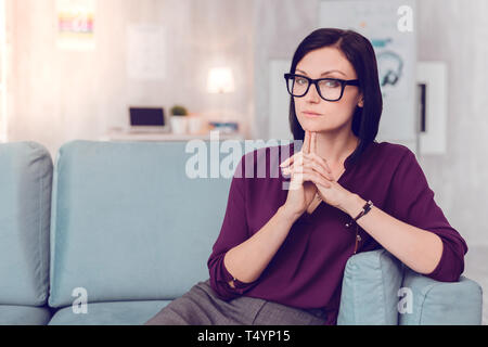 Thoughtful bewitching serious woman having a seat on a couch Stock Photo
