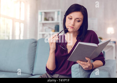 Concentrated stylish charming mid-aged lady holding a book in hands Stock Photo