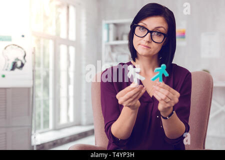 Displeased upset attractive dark-haired woman holding human stick figures Stock Photo
