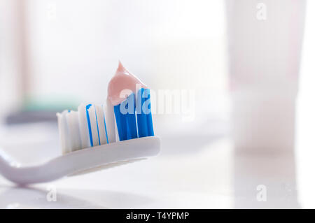 Toothbrush with pink toothpaste on the bathroom sink with dispenser in the background Stock Photo