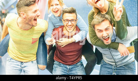 Group of friends having fun in a underground station - Men piggybacking their girlfriends - Young people making party Stock Photo