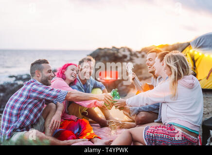 Group of friends cheering with beers outdoor - Happy people camping with tent and making a barbecue having fun toasting bottles of beer Stock Photo