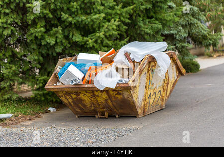 Overflowing rusty metal container for construction waste with cardboard boxes and other plastic trash Stock Photo