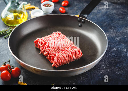 Fresh raw minced beef in frying pan and ingredients over dark background. Stock Photo