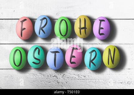 FROHE OSTERN, German for happy easter, written on colored easter eggs against rustic white wooden table Stock Photo