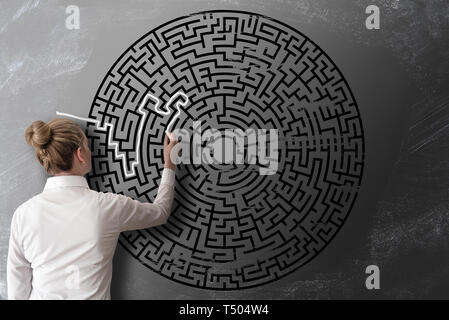 read view of woman trying to find way through chalk drawing of maze on blackboard challenge concept Stock Photo